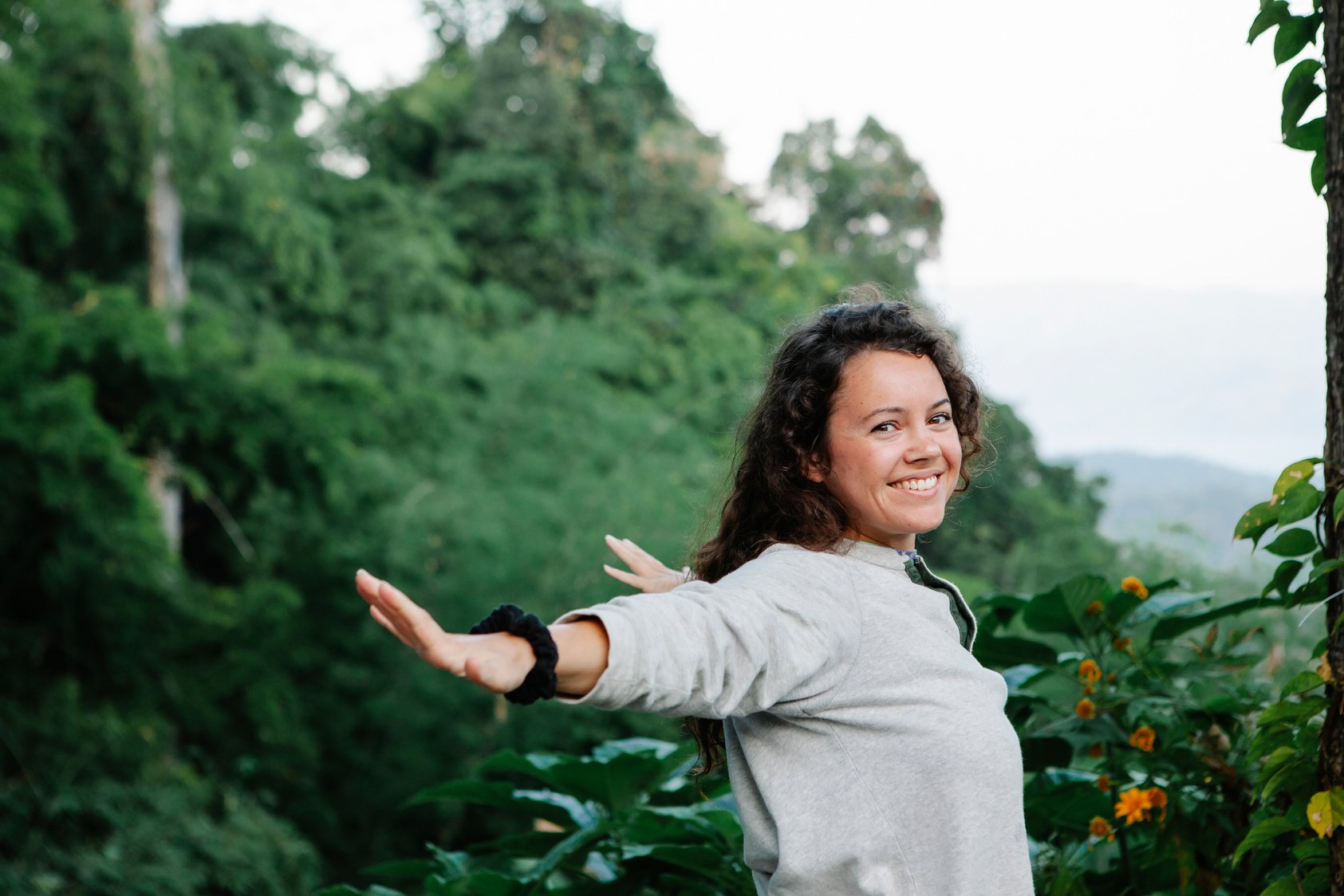 Young happy woman with arms outstretched smiling among green trees